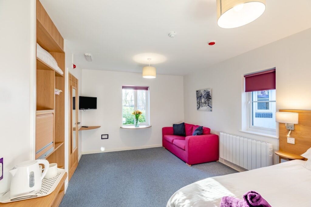 Bedroom with pink sofa, bed, kettle, and storage in a cottage